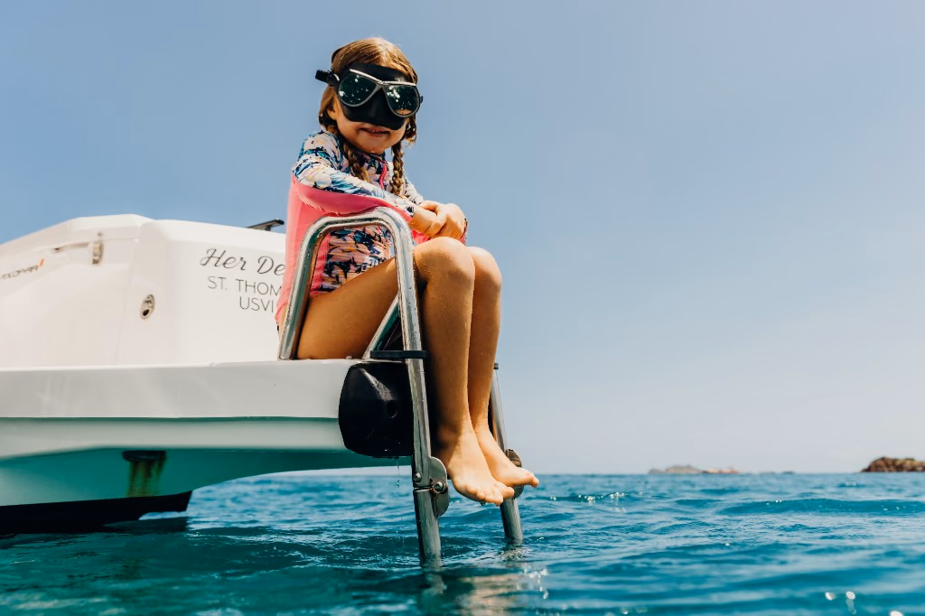 Girl in a snorkel mask sitting on the swim ladder of Her Deal in St. Thomas