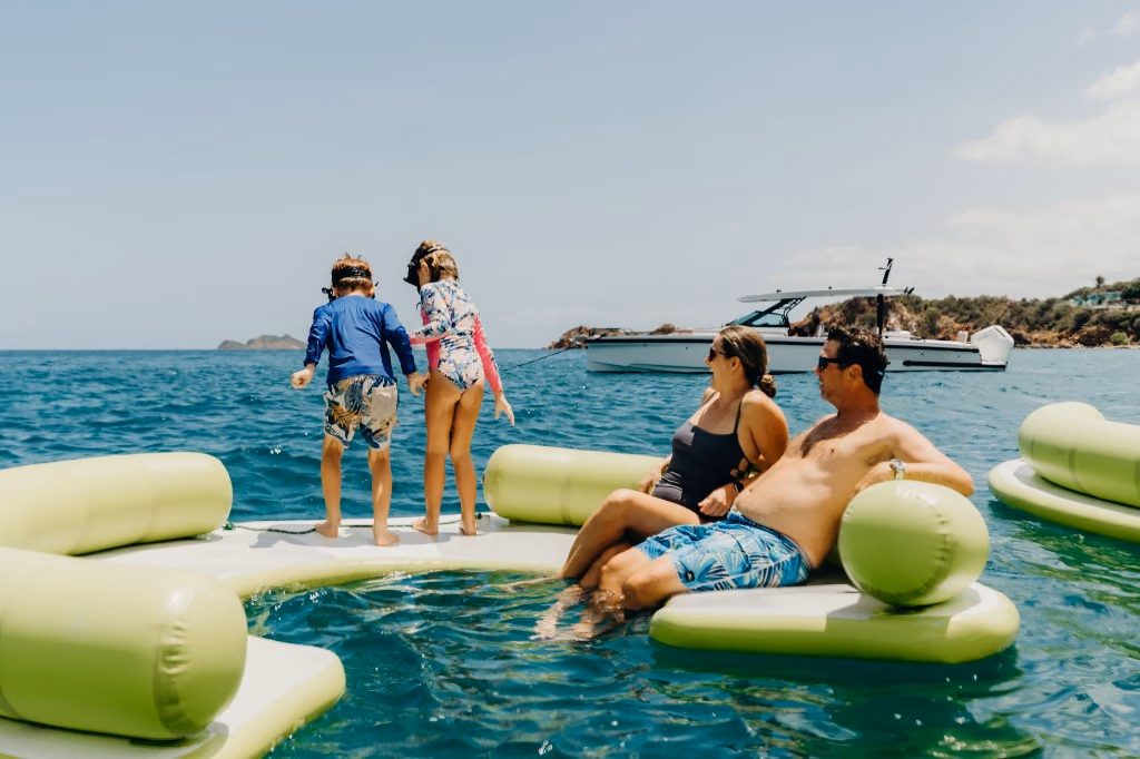 Kids playing on floating platforms while parents relax in the water near Her Deal
